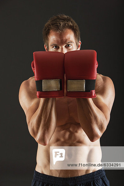 Barechested Boxer  der Handschuhe vor dem Gesicht in defensiver Position hält.