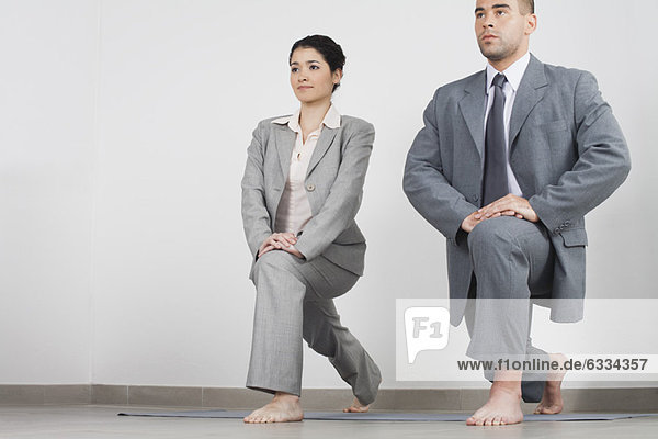 Junge Geschäftsfrau und Geschäftsmann bei der Yoga-Longe Seite an Seite im Büro