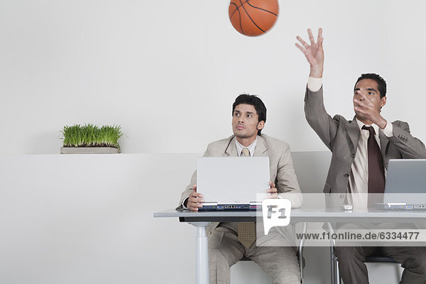 Junger Geschäftsmann beobachtet Kollege beim Basketball-Werfen