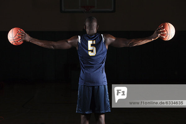 Basketball player holding basketballs in both hands  rear view