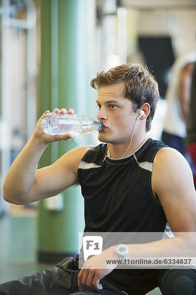 Young man drinking bottled water in gym room