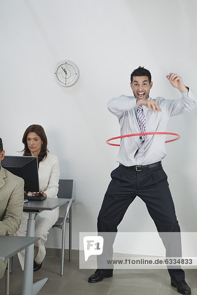 Young businessman playing with hula hoop in office while colleagues work