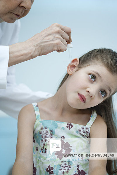 Arzt setzt Ohrentropfen ins Ohr des Mädchens