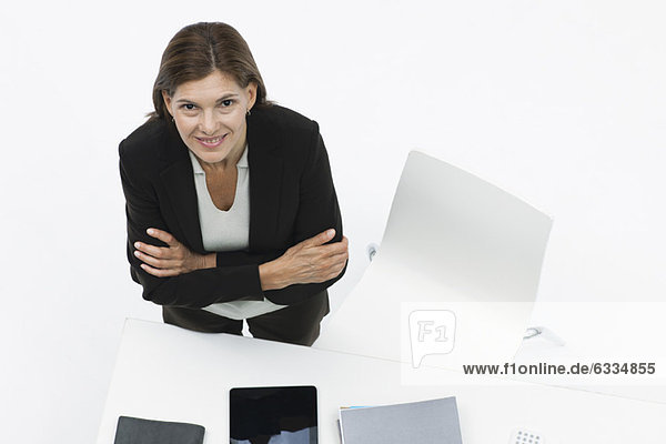 Businesswoman standing by desk with arms folded