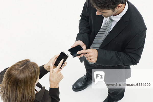 Geschäftsfrau und Geschäftsmann von Angesicht zu Angesicht  beide mit Hilfe von Smartphones