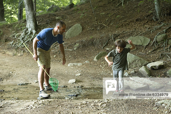 Vater und Sohn im Wald  Junge springt über den Bach