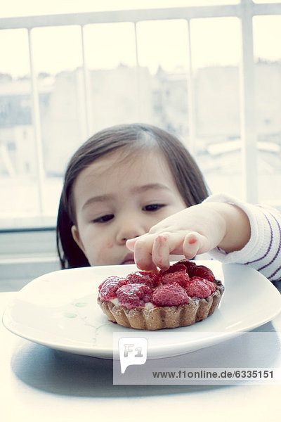 Kleines Mädchen steckt Finger in Obstkuchen