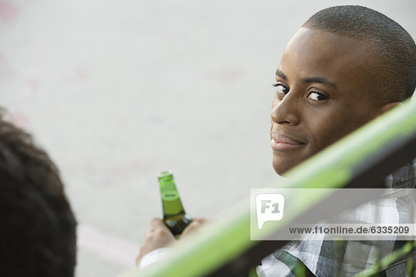 Junger Mann hält Bierflasche  schaut über die Schulter