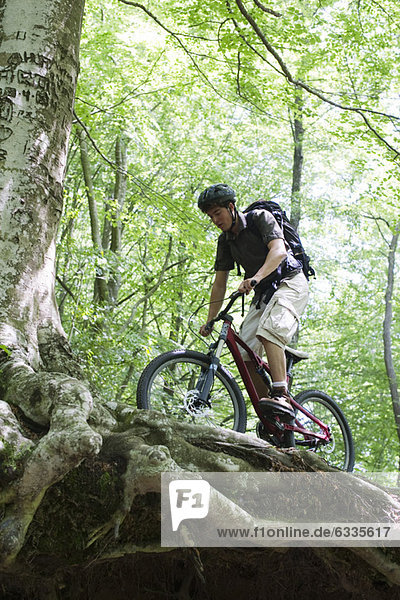Young man riding bicycle in woods  low angle view