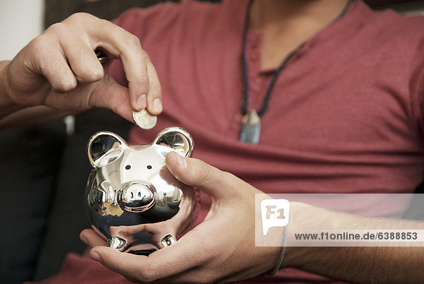 Teenager-Junge der Geld ins Sparschwein steckt.