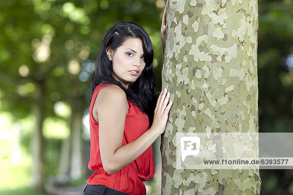 Junge Frau mit rotem Top lehnt sich an Baum