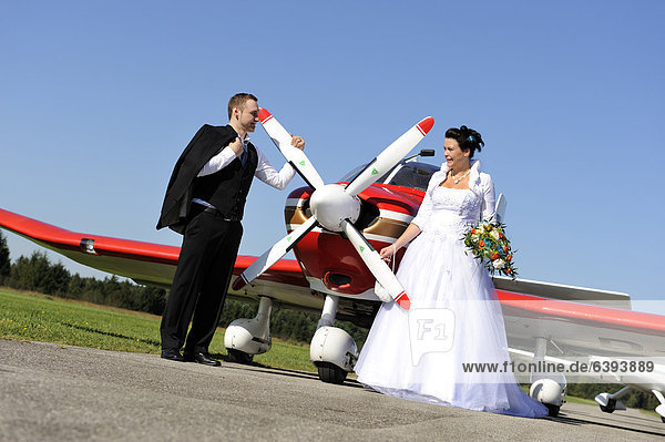 Junges Brautpaar posiert vor einem Propellerflugzeug