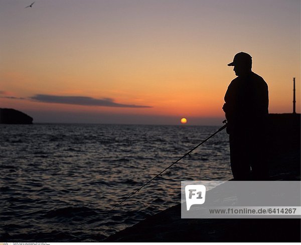 Ein Angler bei Sonnenuntergang Mullion Cove Cornwall England