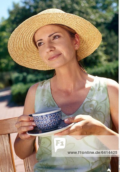 Eine Frau sitzt im Garten und trinkt Kaffee