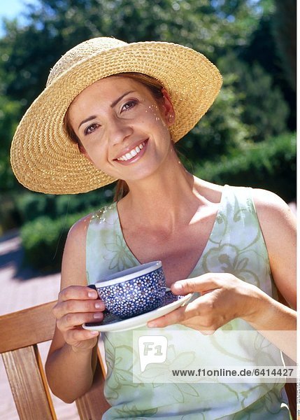 Eine Frau sitzt im Garten und trinkt Kaffee