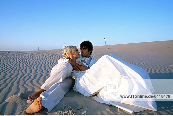 Hochzeitspaar liegt im Sand