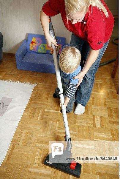 Kleiner Junge hilft seiner Mutter beim Staubsaugen