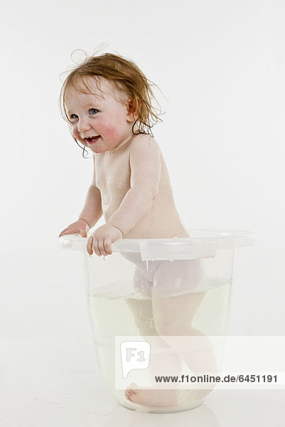 Ein kleines Mädchen  das in einem Eimer mit Wasser steht.
