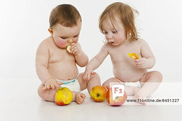 Zwei kleine Mädchen sitzen zusammen und essen Äpfel.