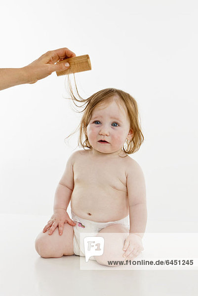 Ein kleines Mädchen  das sich die Haare kämmen lässt.