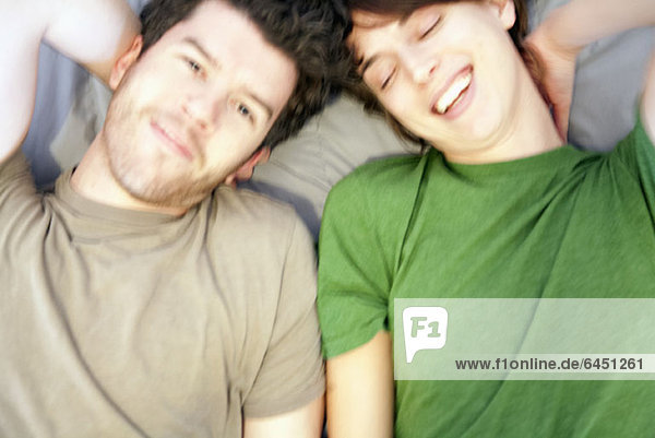 A young couple lying on a bed side by side  laughing  close-up
