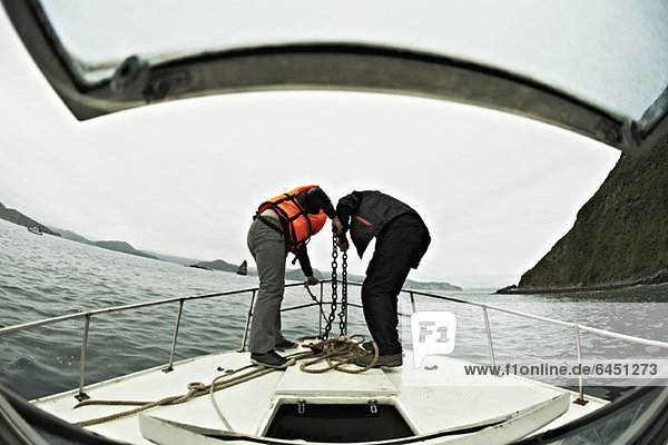 Zwei Personen,  die einen Anker vom Bug eines Bootes senken,  Avacha Bay,  Russland