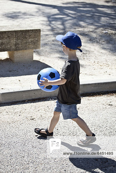 A young boy walking with a ball