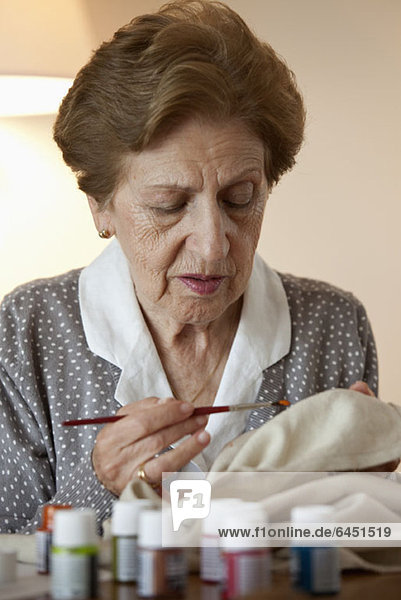 A senior woman painting on fabric