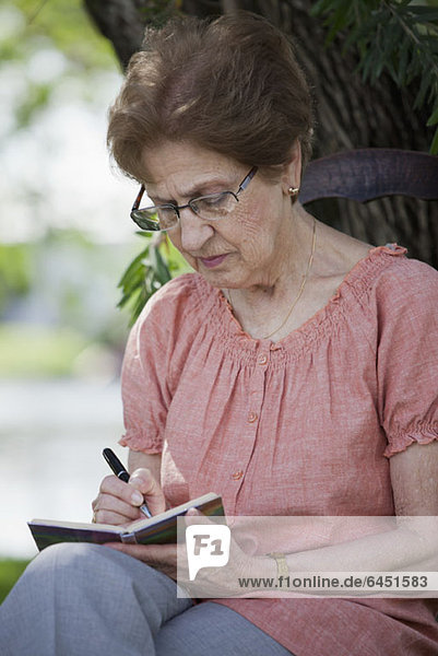 Eine ältere Frau  die in einem Buch schreibt.