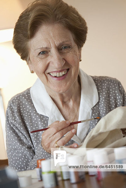 Eine ältere Frau malt auf Stoff