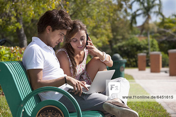 Ein junges Paar auf einer Parkbank mit Laptop und Mobiltelefon