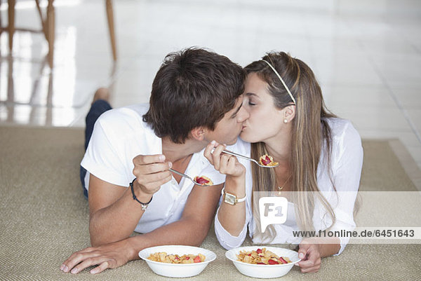 A young couple kissing while eating breakfast