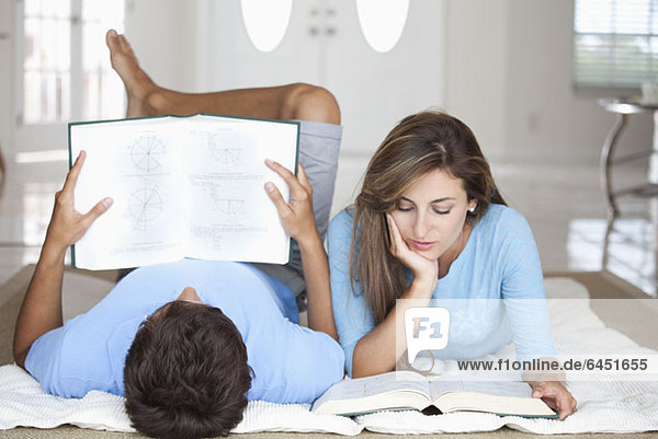 Ein junges Paar liegt auf dem Boden und liest Lehrbücher.