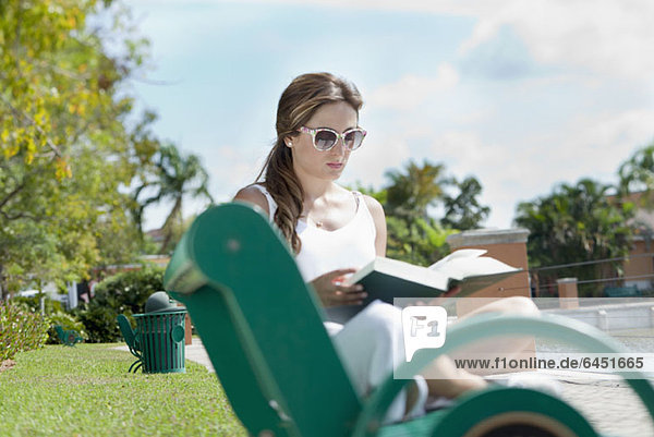Eine Frau liest ein Buch auf einer Parkbank.