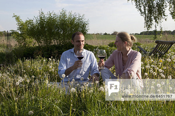 Ein Paar sitzt im Gras und genießt etwas Rotwein.
