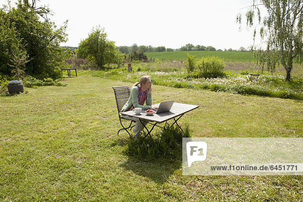 A woman with a laptop sitting at a table in her back yard  rural setting