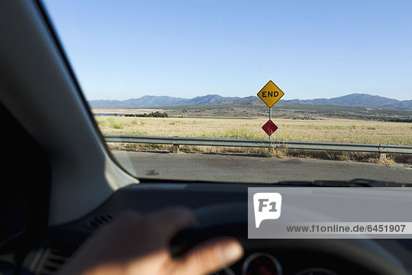 View through a car windshield of an END road sign and mountain ranges behind
