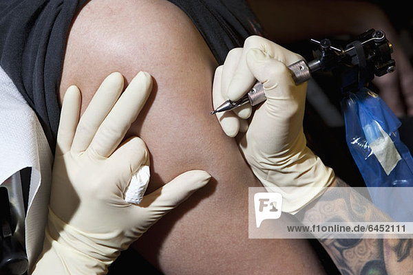 A tattoo artist preparing to tattoo a man's bare arm  close-up