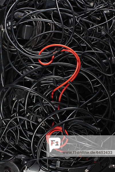 A single red cord in the form of a question mark amongst a tangle of black cords and cables