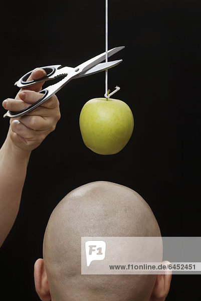 Eine Frau schneidet einen Apfel an einer Schnur über dem Kopf eines Mannes.
