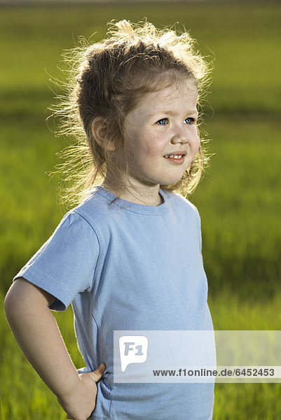 Ein junges Mädchen steht auf einem Feld und schaut weg.