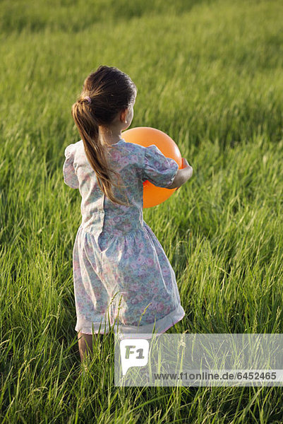 Rückansicht eines Mädchens  das einen Ballon auf einem Feld hält.