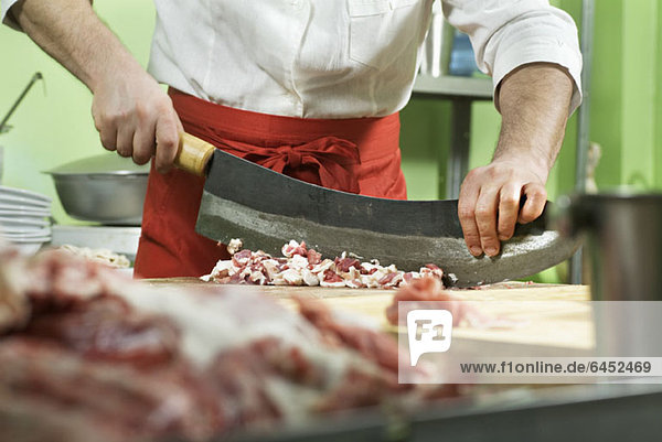 Detail eines Mannes  der mit einem großen Messer Fleisch zerkleinert.