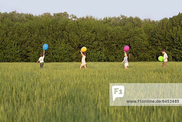 Kinder  die mit Luftballons auf einem Feld spazieren gehen.