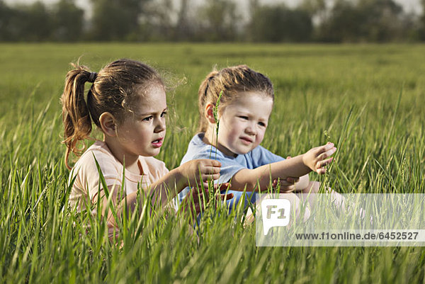 Zwei junge Mädchen  die auf einem Feld sitzen.