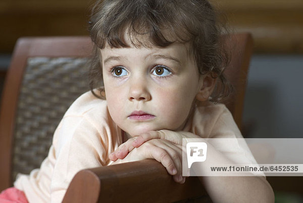 Ein junges Mädchen sitzt auf einem Stuhl und schaut weg.
