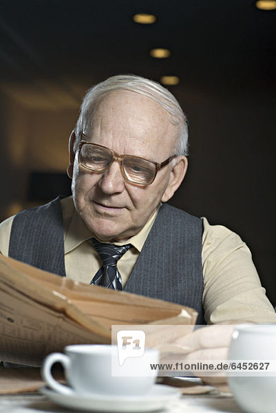 Ein älterer Mann  der eine Zeitung in einem Café liest.