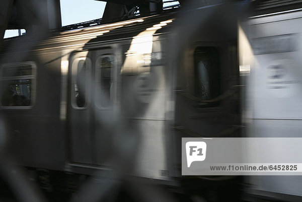American public transport train passing by with blurred wire mesh fence in foreground