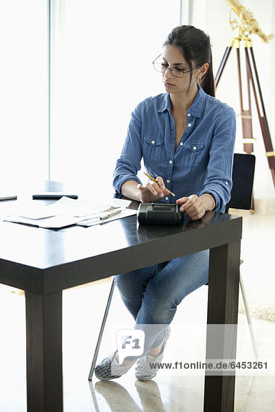 Frau mit Taschenrechner am Schreibtisch