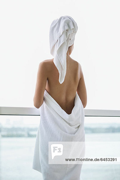Frau in Handtuch gewickelt mit Blick vom Balkon auf das Meer